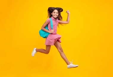 Schoolgirl in school uniform with backpack. Teenage girl student on yellow isolated background. Crazy run and jump. Learning and education children