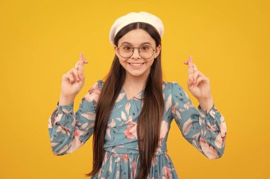 Şans dilemek için şans dileyen genç bir çocuk. Kız dua ediyor ve rüyalarının gerçekleşmesini umuyor, sarı arka planda izole bir şekilde. Mutlu ergen, pozitif ve gülümseyen duygular