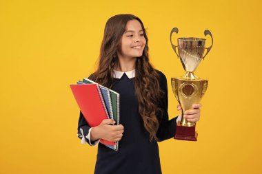 Okul üniformalı kız zaferi ödülle kutluyor. Sarı arka planda ödül kazanan gençler var. Çocuk kitapları altın kupayla ya da kazanan kupayla tutuyor. Eğitim mezuniyeti, zafer