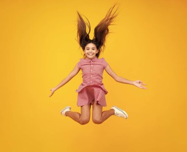 Amazed teen girl. Full size photo of positive teen girl jump with movement summer dress, fashion kids outfit isolated over yellow background. Teenager face with crazy movement hair