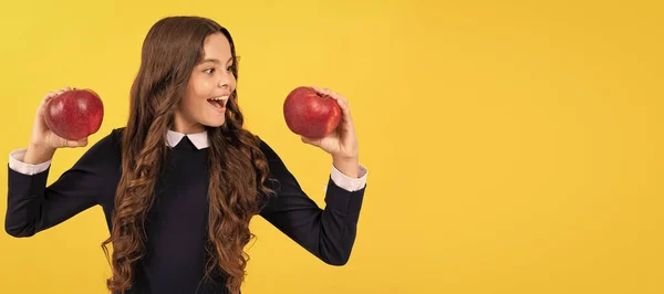 stock image happy teen girl choosing red vitamin apple for lunch on yellow background, choice. Child girl portrait with apple, horizontal poster. Banner header with copy space