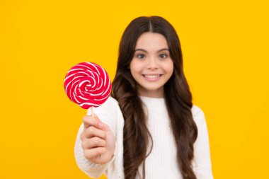 Genç kız sarı arka planda lolipop karamel tutuyor, şekerci dükkanı. Tatlılı ergen enayiler. Mutlu yüz, pozitif ve gülümseyen genç kız duyguları