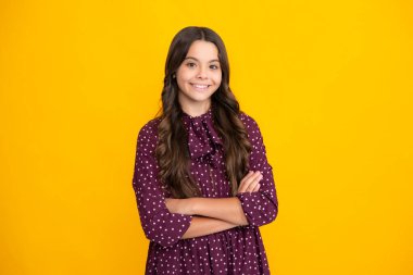 Teenage girl kid with crossed arms, looking at camera, isolated on yellow studio background