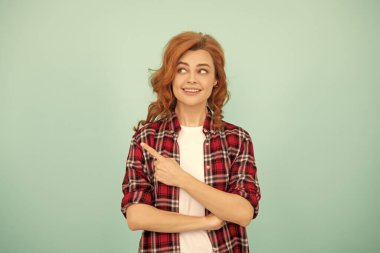 Mavi arka planı gösteren kareli tişörtlü mutlu kızıl kadın..