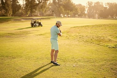 Golf sopasıyla şapkalı bir golfçü. İnsanların yaşam tarzı. Adam yeşil çimlerde oyun oynuyor. Yaz etkinliği. Profesyonel açık hava sporu. Spor giyim. Profesyonel golf sahasında erkek golfçü.