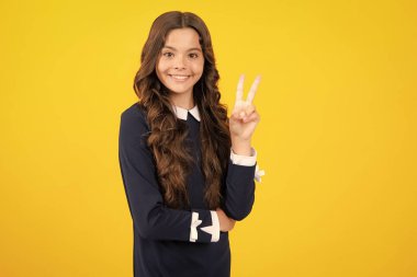 İzole edilmiş sarı arka planda duran genç kız parmaklarını zafer işareti yaparken gösteriyor. İki numara, v işareti.