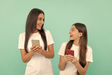 amazed mother and daughter chatting on smartphone on blue background. clipart