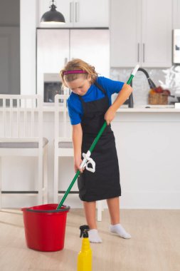 Çocuk ev işlerine yardım ediyor, temizlik yapıyor. Çocuk ev konseptiyle temizlik yapıyor. Ev işlerine yardım etmek için paspasla çocuk temizliği. Küçük sevimli çocuk mutfak arka planında temizlik yapıyor.