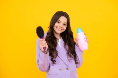 Sarı arka planda şampuan şişesi ya da duş jeli olan genç bir kız çocuğu. Çocukların saçı kozmetik üründür. Mutlu yüz, pozitif ve gülümseyen genç kız duyguları