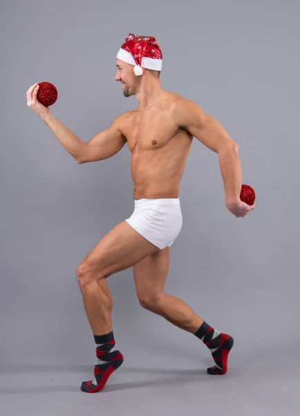 疯狂的桑塔 可笑的肌肉男 戴着桑塔帽 穿着白色内裤 圣诞节和新年的概念 赤裸裸的同性恋桑塔在灰蒙蒙的工作室背景下的滑稽姿势 — 图库照片