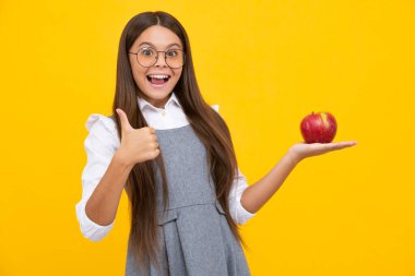 Child girl eating an apple over isolated yellow background. Tennager with fruit. Happy girl face, positive and smiling emotions