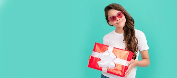 fashionable happy kid in sunglasses hold gift box, birthday. Kid girl with gift, horizontal poster. Banner header with copy space
