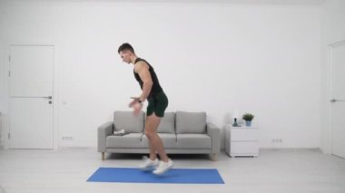 Fitness sporcusu atlama egzersizleri yapıyor. Atlama hamleleri yapan formda bir sporcu. Evde fitness var. Spor egzersizleri spor salonunda. Evde spor yapma rutini. Spor ve zindelik.
