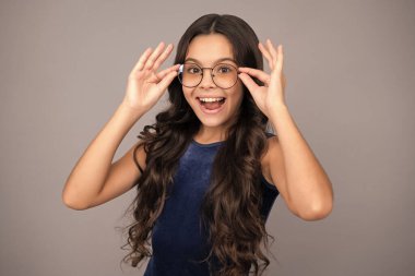 Excited face, cheerful emotions of teenager girl. Teenager child wearing glasses on gray studio background. Cute girl in eyeglasses