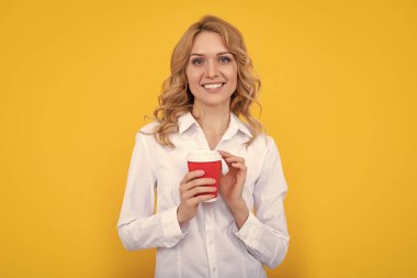 Sarı arka planda kahve fincanı olan pozitif sarışın kadın..