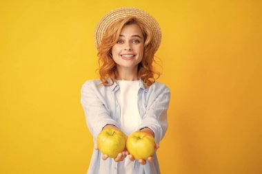 Sağlıklı dişleri olan, yaz hasır şapkalı, gülümseyen kızıl kadın elma tutuyor. Stüdyoda izole edilmiş