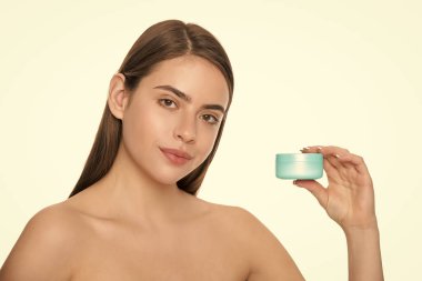 Beyaz arka planda cilt için krem kavanozu gösteren genç bir kadın. Fotokopi alanı ve güzellik..