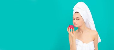 Havlu giymiş güzel bir kadın mavi arka planda cilt kremi kokusu alıyor. Güzel kadın, izole edilmiş yüz portresi, taklit alanı olan pankart.