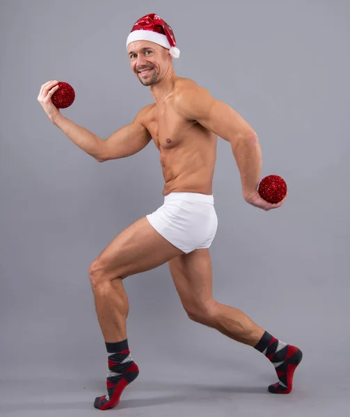 可笑的肌肉桑塔在桑塔的帽子和白色内裤 圣诞节和新年的概念 赤裸裸的同性恋桑塔在灰蒙蒙的工作室背景下的滑稽姿势 — 图库照片