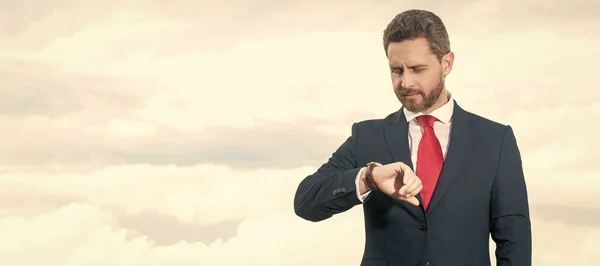 Stock image businessman in businesslike suit checking time on sky background. Man face portrait, banner with copy space