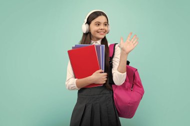 Okul çocuğu, kulaklıkları ve mavi izole stüdyo geçmişine sahip okul çantalı genç kız. Çocuk okulu ve eğitim konsepti