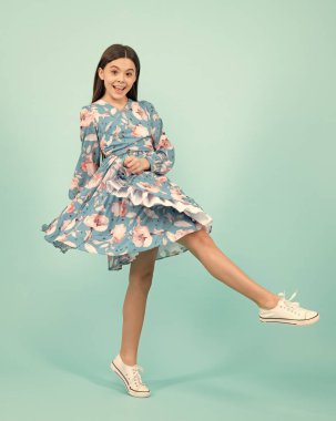 Elegant teenager child girl in fashion dress. Girl in cotton dress isolated on blue background. Excited teenager, amazed and cheerful emotions