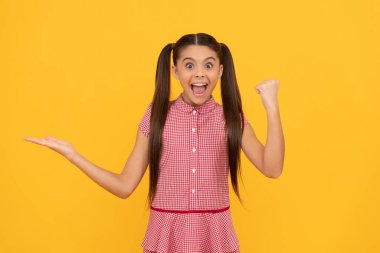 Şaşırmış genç kız sarı arka planda ürün sunuyor fotokopi alanı başarıyı ve terfiyi kutluyor.