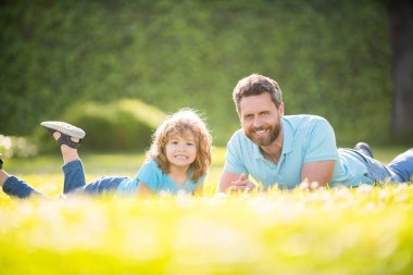 Çocukluk ve ebeveynlik. Ebeveyn, küçük çocuk çimlerin üstündeyken rahatlar. İyi ki babası yaz günü çocuklu. Ebeveynlik ve babalık. Babalar günü. Mutlu baba ve oğul parkta eğleniyor. aile değeri.