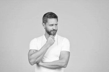 Serious thoughtful man in white tshirt stroke chin thinking grey background, think.