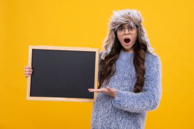 Kara tahtalı, kışlık şapkalı küçük bir kız. Liseli kız fotokopi odası ve okul satışı için karatahta tutuyor. Genç bir kız öğrencinin portresi. Şaşırmış yüz, genç kızın sürprizi.