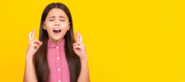 Glad teenager girl crosses fingers, closes eyes with pleasure, anticipate hearing good news. Child face, horizontal poster, teenager girl isolated portrait, banner with copy space