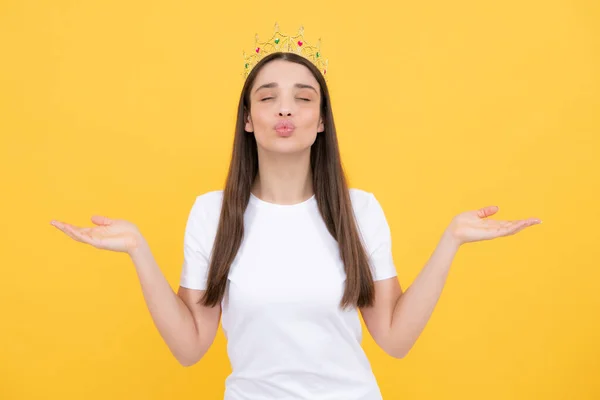 Pretty young woman wear crown, isolated on yellow color background. Girl with golden crown, arrogance and privileged status, concept of success and dreams