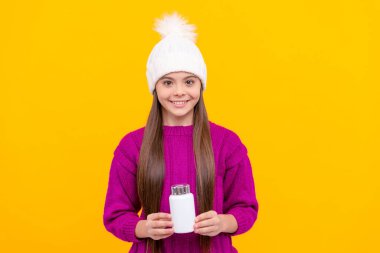 Doğal hap ürünleri olan genç bir kız. Vitamin ürünü sunuyorum. Çocuklar için multivitamin tableti. Sağlıklı bir yaşam tarzı. Çocukluk sağlığı. Haplı, kışlık şapkalı neşeli çocuk. yiyecek takviyesi.