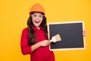 Atölyedeki ressam. Yenileme ve onarım. Kasklı, fırçalı genç bir kız. Kasklı çocuk. İnşaat alanında boyacı çocuk. Heyecanlı genç kız