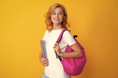 Eğitim, eğitim, üniversite, sarı arka plan üzerine üniversite konsepti. Sırt çantası ve not defteriyle gülümseyen güzel bir kadın öğrencinin portresi.