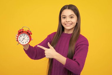 Portrait of teenage girl with clock alrm, time and deadline. Studio shot isolated on yellow background