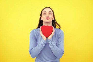 Sarı arka planda sevgililer günü hediyesi tutan güzel bir kız. Elinde kırmızı kağıt kalp tutan genç bir kadının portresi. Mutlu kadınlar için aşk sembolleri, sevgililer günü ya da doğum günü