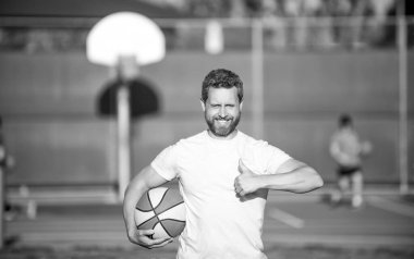 Neşeli kaslı erkek sporcu basketbol oyuncusu topu açık havada tutuyor başparmak hareketi ve spor başarısı gösteriyor..