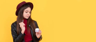 Şapkalı pozitif çocuk makyaj fırçası ve sarı arka planda pudra tutuyor. Genç çocuklar için makyaj malzemeleri, poster tasarımı. Güzellik çocukları makyaj, fotokopi alanı ile pankart