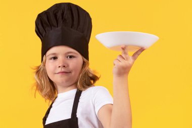 Funny child cook with cooking plate. Child chef cook. Child wearing cooker uniform and chef hat preparing food, studio portrait clipart