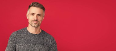 Man face portrait, banner with copy space. positive grizzled guy in sweater on red background,