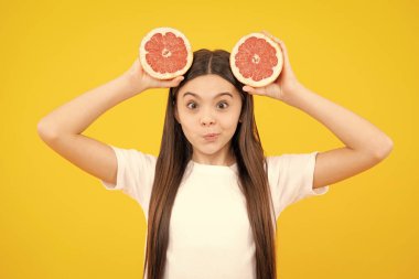 Teenage girl holding a grapefruit on a yellow background. Funny face