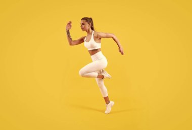 Sarı arka planda spor kıyafetlerine atlayan fitness kızı..