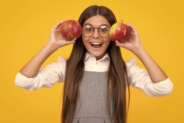 Child girl eating an apple over isolated yellow background. Tennager with fruit. Happy girl face, positive and smiling emotions