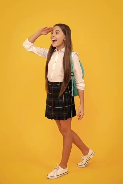 幸せな子供でバックパックで学校の制服の完全な長さ上の黄色の背景遠く見て — ストック写真