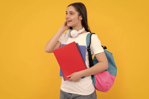 バックパックとヘッドフォンを持つ幸せな若い女の子は黄色の背景 知識に関するワークブックを保持します — ストック写真