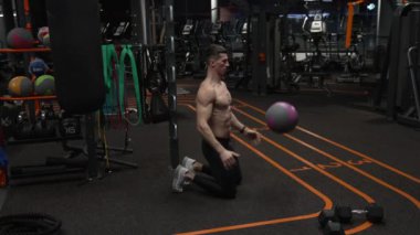 Diz çöküp spor salonuna fitness topu atan adam. Formda sporcu spor salonunda topla egzersiz yapıyor. Spor salonunda top egzersizi. Formunu geliştiriyor. Yavaş çekim.