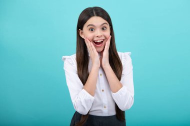 Heyecanlı bir yüz. Şaşırtıcı bir ifade, neşeli ve mutlu. Mavi arka planda çocuk stüdyosu portresi. Çocukluk yaşam tarzı konsepti. Sevimli genç kız yüzü. Yakından.