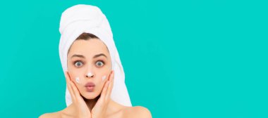 Cilt bakımlı güzel kadın. Şaşırmış genç kız mavi arka plana yüz kremi sürmüş. Güzel kadın, izole edilmiş yüz portresi, taklit alanı olan pankart.