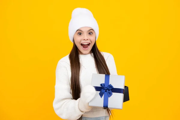 New Year or Christmas holiday gift. Portrait of a teenager child girl holding present box isolated over yellow studio background. Present, greeting and gifting concept. Birthday holiday concept